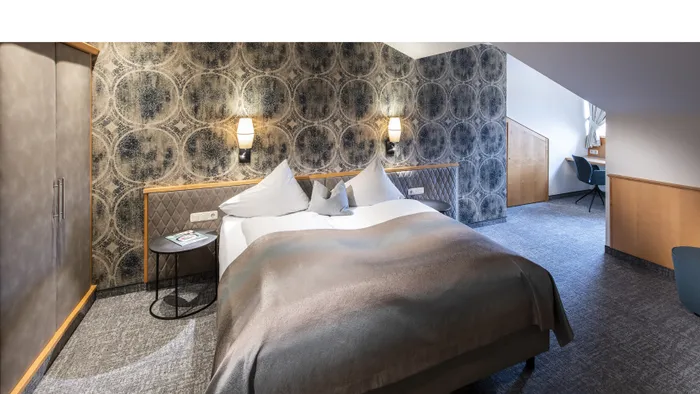 Modernes Hotelzimmer mit Doppelbett, stilvoller Tapete und gemütlichem Schreibtisch unter Dachschräge